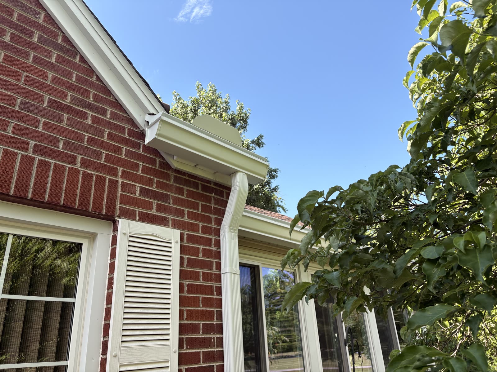 New white seamless gutter installed along the roofline of a red brick home