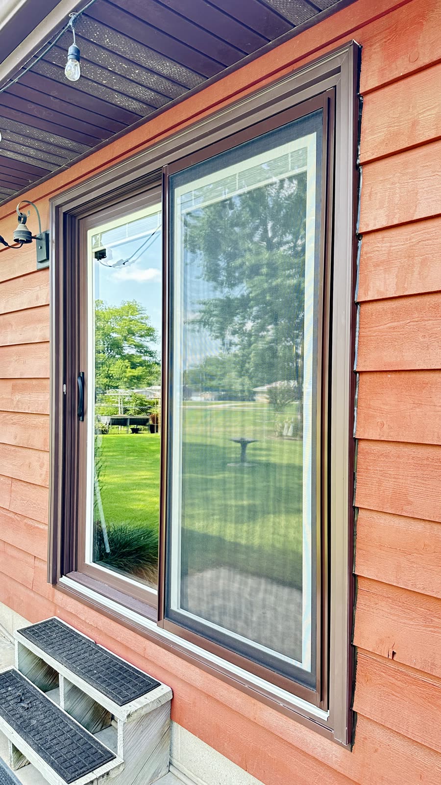 Bronze sliding patio door with screen installed in red siding