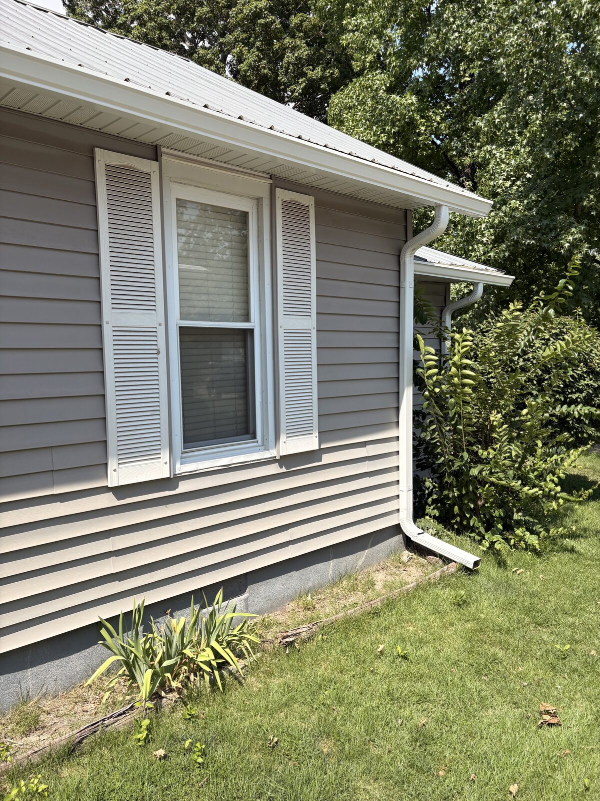 White seamless gutter installed above a window on a tan sided home