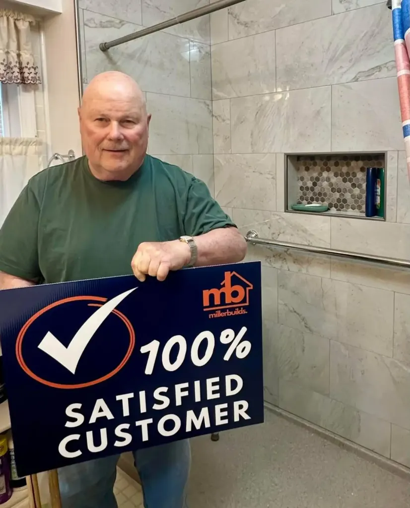 Miller Builds customer holding a 100% Satisfied Customer sign in his remodeled walk-in shower