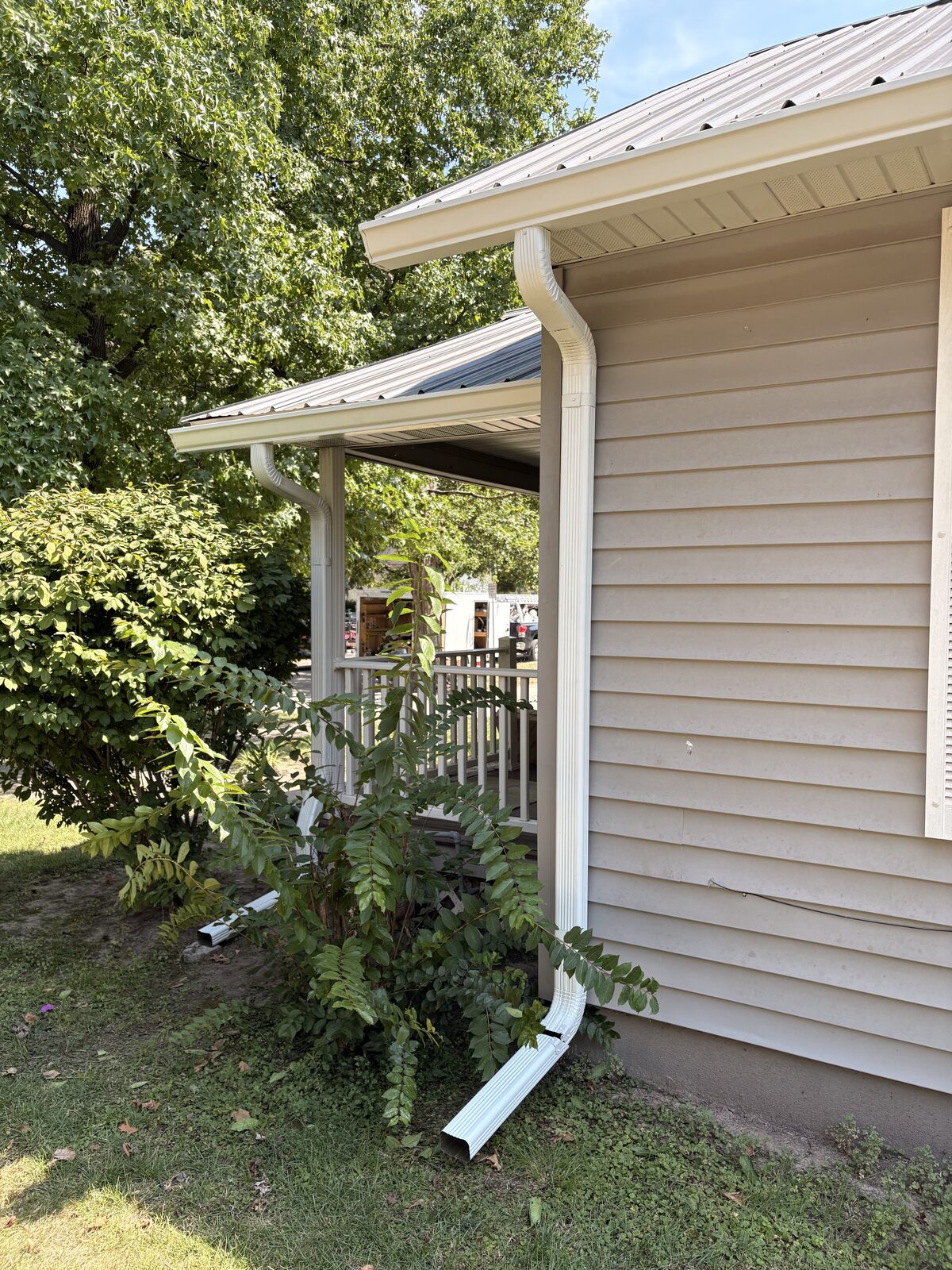 New white gutter and downspout on the corner of a sided home
