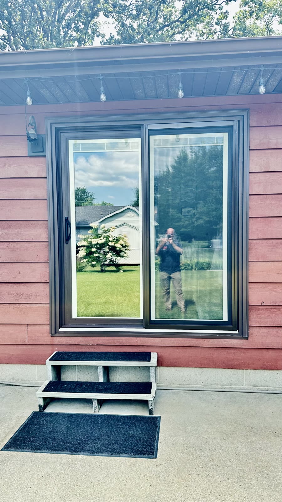 Wide bronze sliding patio door installed in a pink sided home with new trim