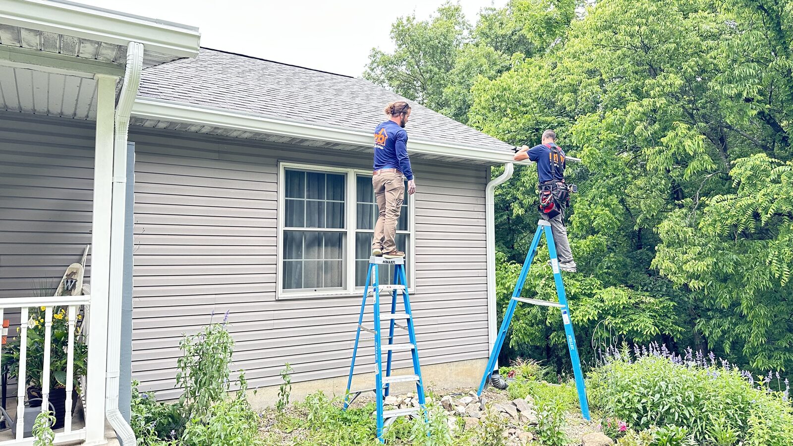 Two Miller Builds installers on ladders hanging seamless gutter on a home