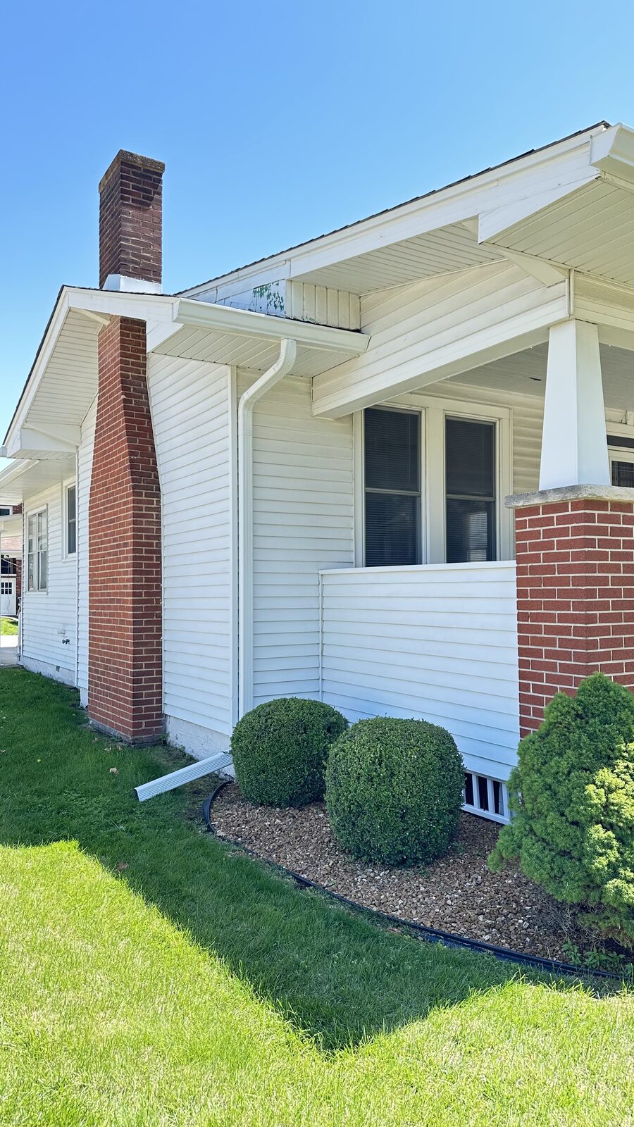 White seamless gutter along the roofline of a white home with a brick chimney