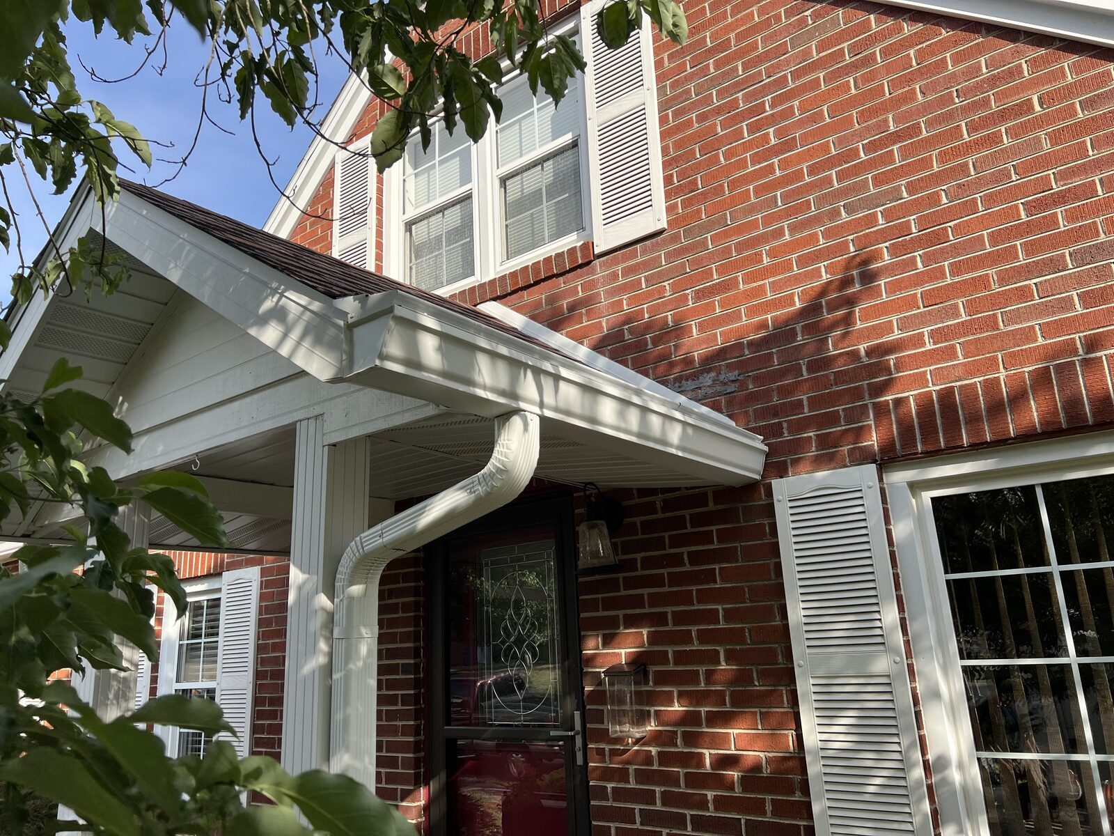 White seamless gutter and downspout on a red brick home with a covered entry